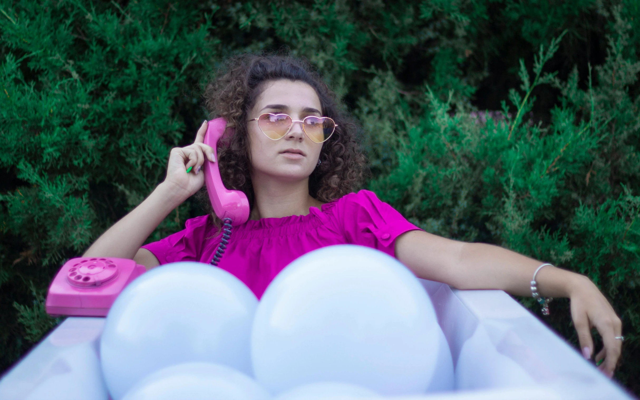 a woman in a pink shirt sits in a cart with balloons and talks on a pink telephone