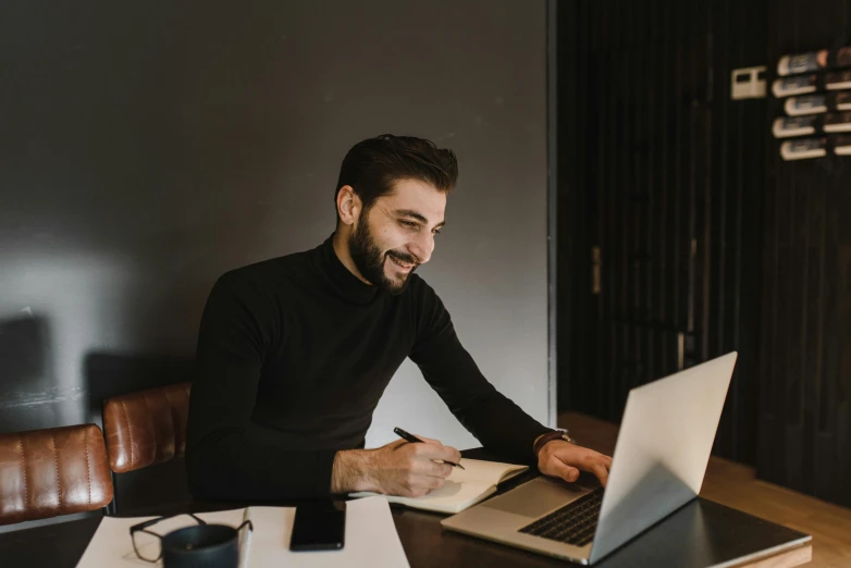 a man wearing a black shirt is on his laptop and smiling