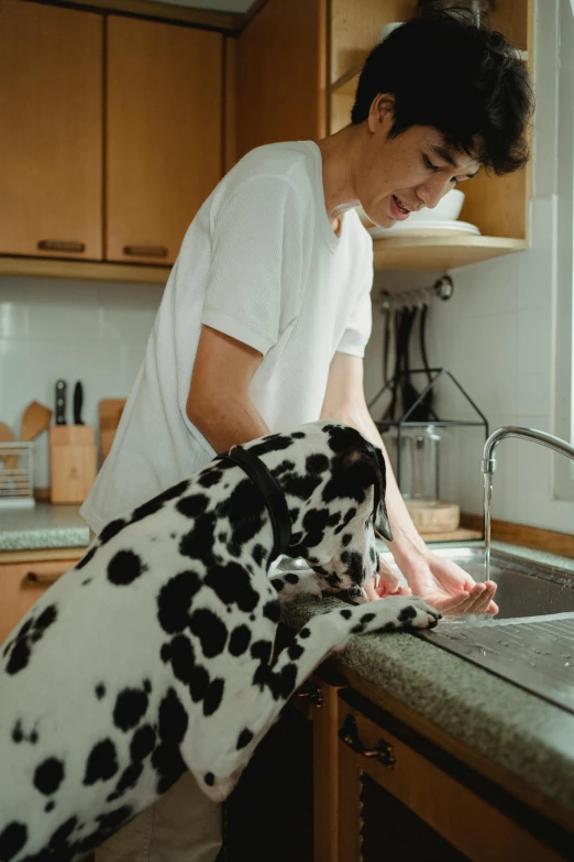 a man in a kitchen holding onto a dog that is sitting in a sink