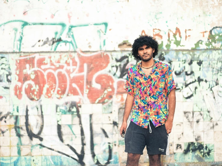 a guy stands in front of a wall covered with graffiti