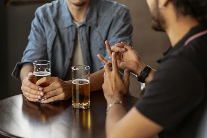 two people sitting at a table talking and drinking beer