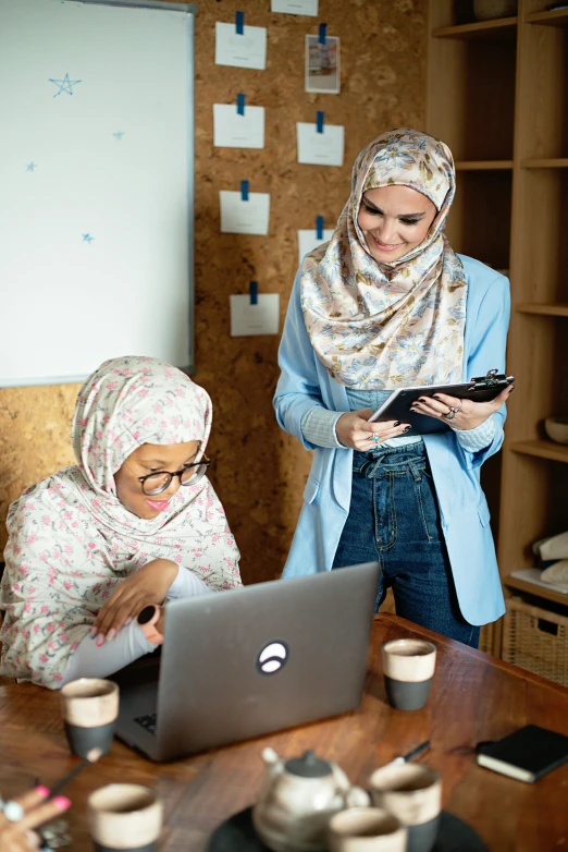 two people look at a computer screen while one woman looks at a piece of paper