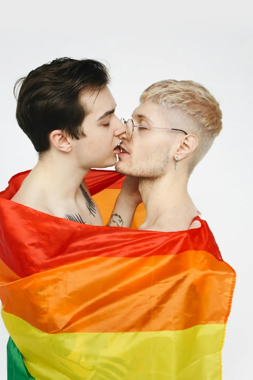 a man standing behind two people wrapped in a rainbow flag