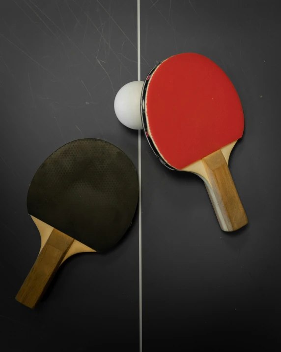 ping pong paddles, and a table tennis ball are sitting on a black surface