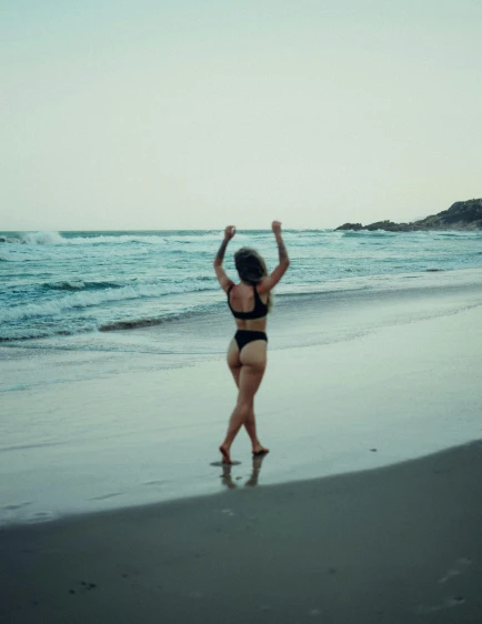 a lady in a bodysuit jumping up at the beach