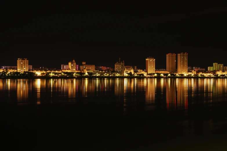 a city at night in the background is reflected in a lake
