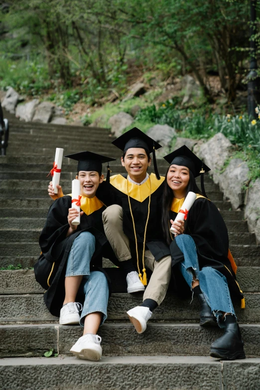 three students sitting down holding their graduation items