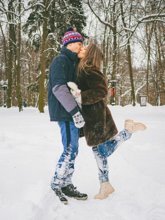 man and woman kissing in snow with trees behind them