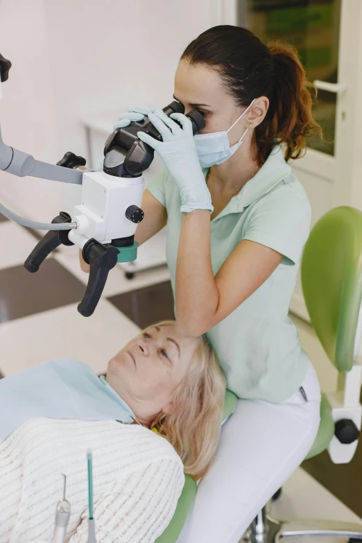a woman sitting in the dentist chair while a woman looks at her phone