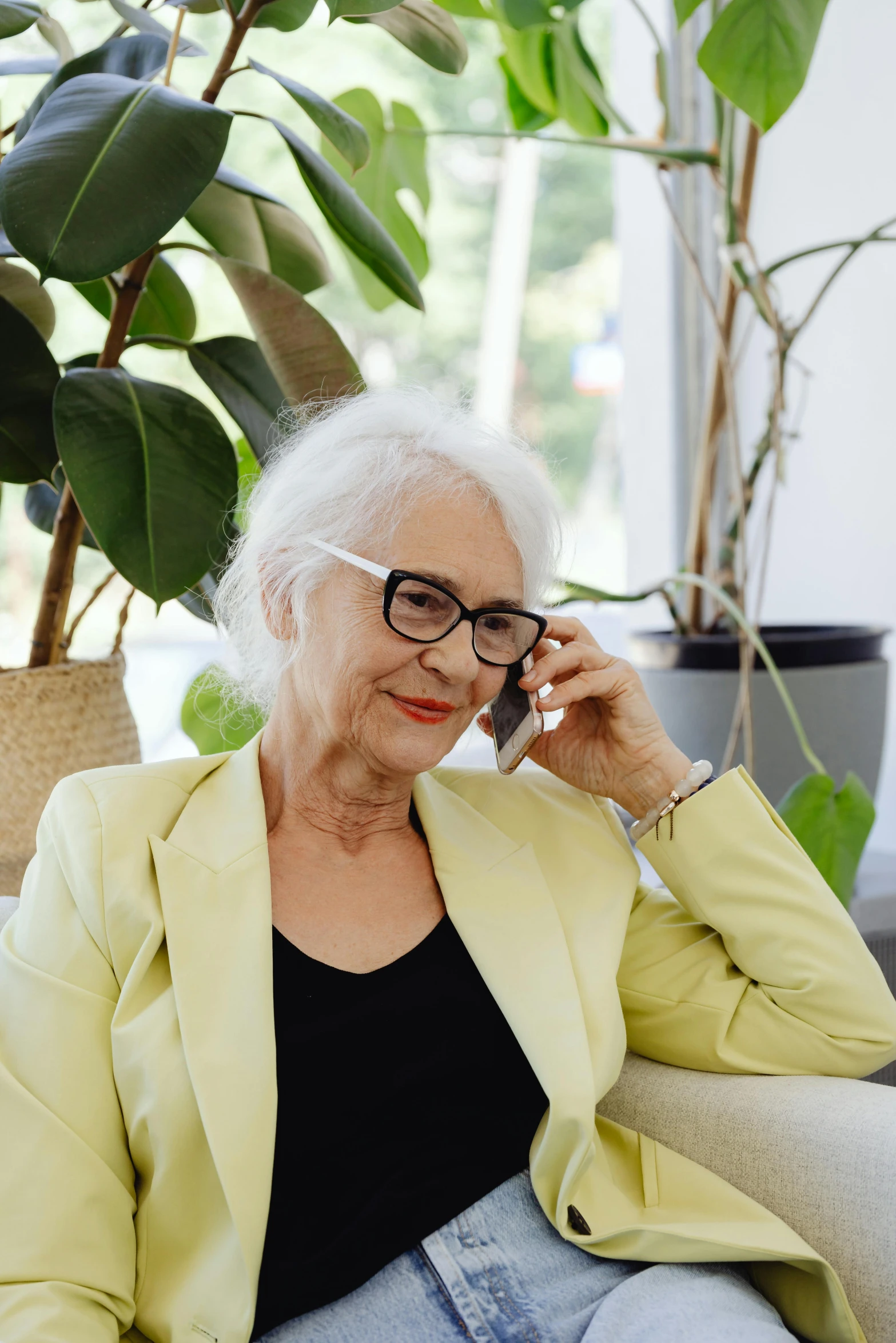 an older woman with eyeglasses sitting on a couch in front of potted plant