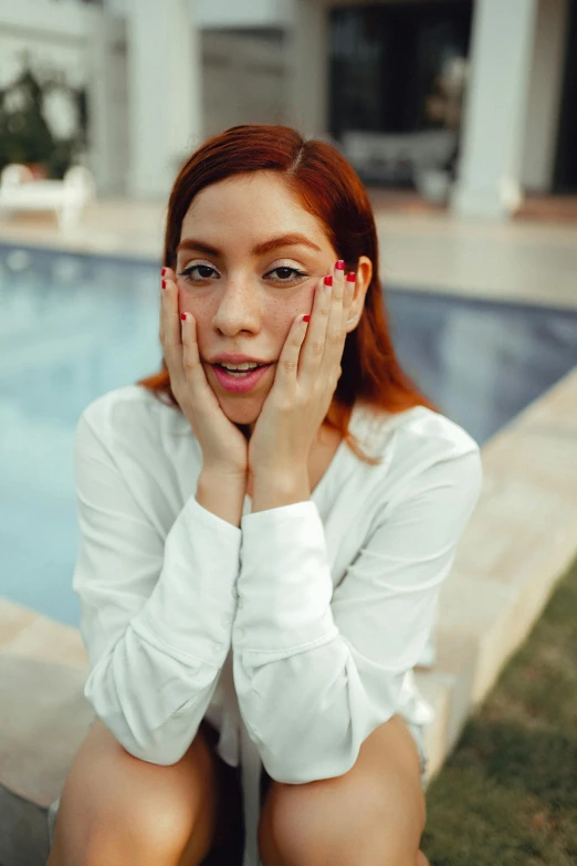 red headed woman leaning on the edge of pool posing for the camera