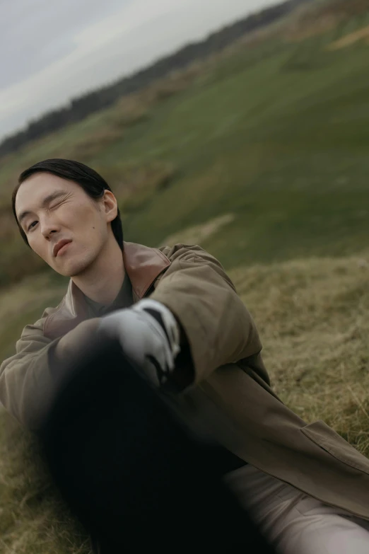 the man sits in a grassy field near a hill