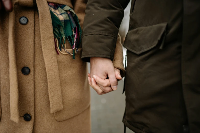 two people holding hands while wearing brown coats