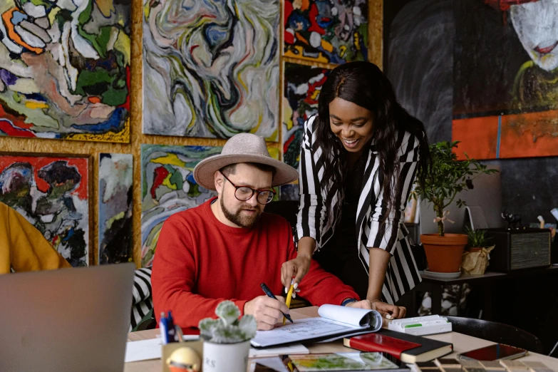 a man and woman sitting at a table working on soing on paper