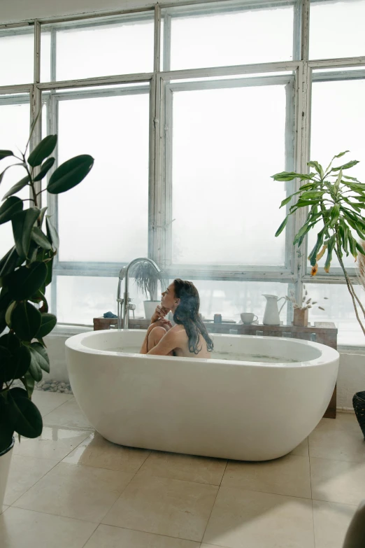 woman laying in the bath tub surrounded by large windows