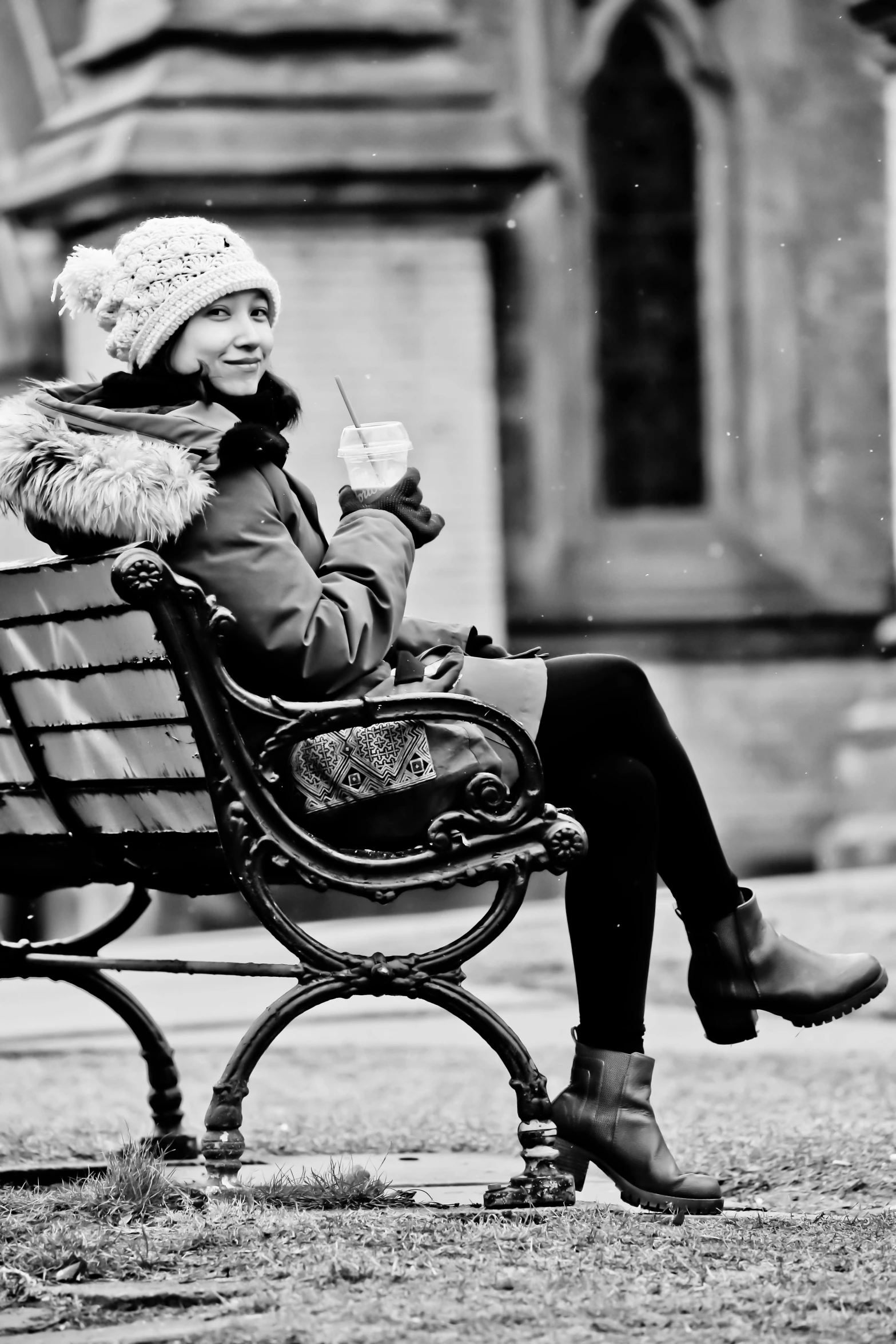 a woman sitting on top of a park bench wearing a hat and holding a cell phone