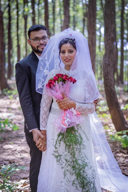 a bride and groom standing in the woods, holding hands