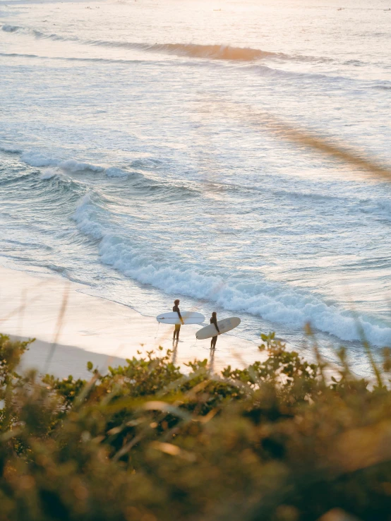 two people walking into the water carrying their surf boards