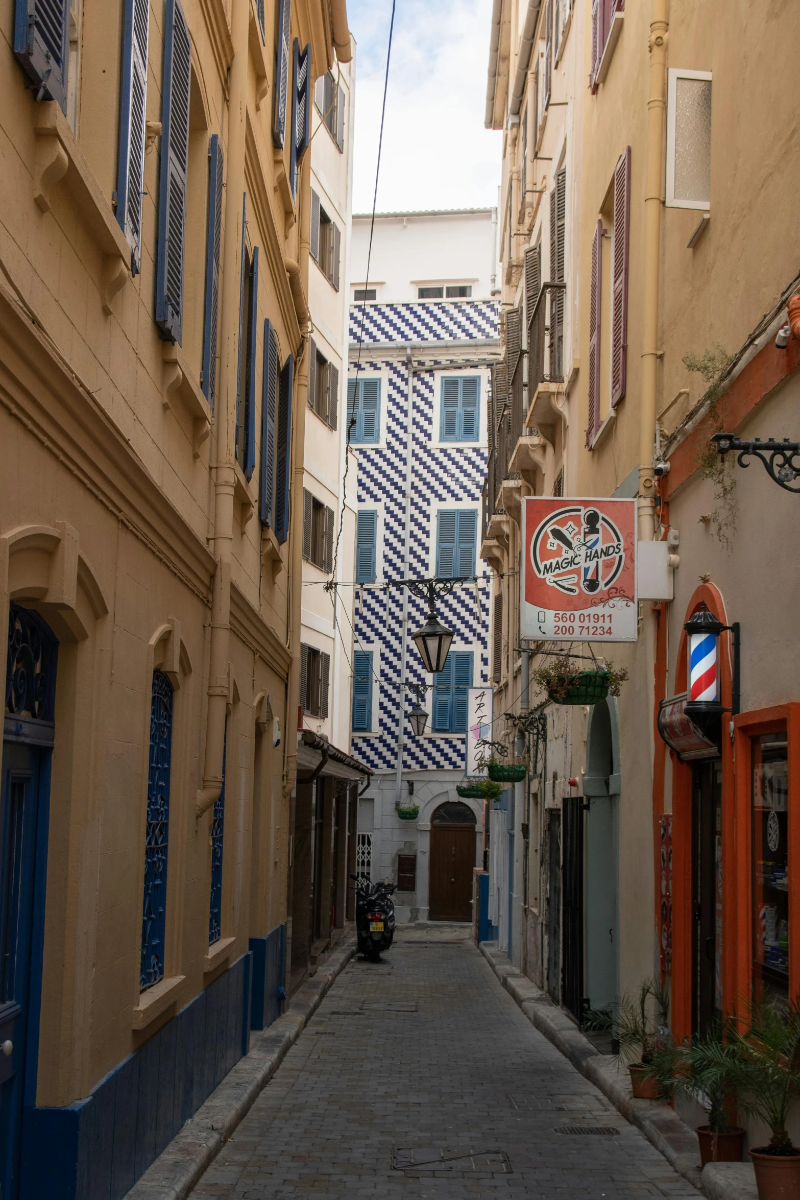 a narrow street with several buildings on both sides and cars parked along the sidewalk