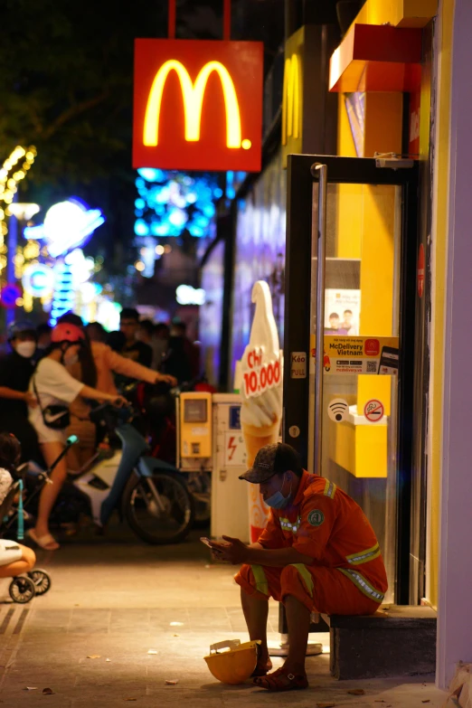 a man sitting in front of a mcdonalds near a neon sign