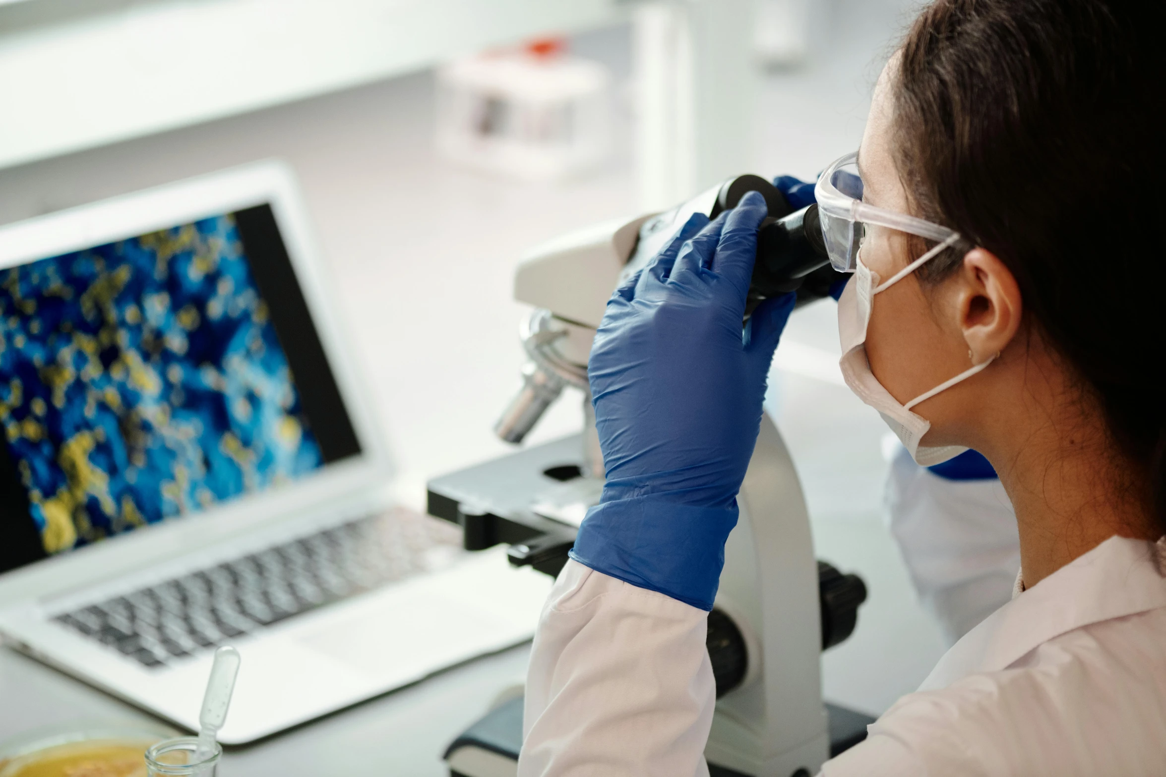 a person wearing a glove looking through a microscope