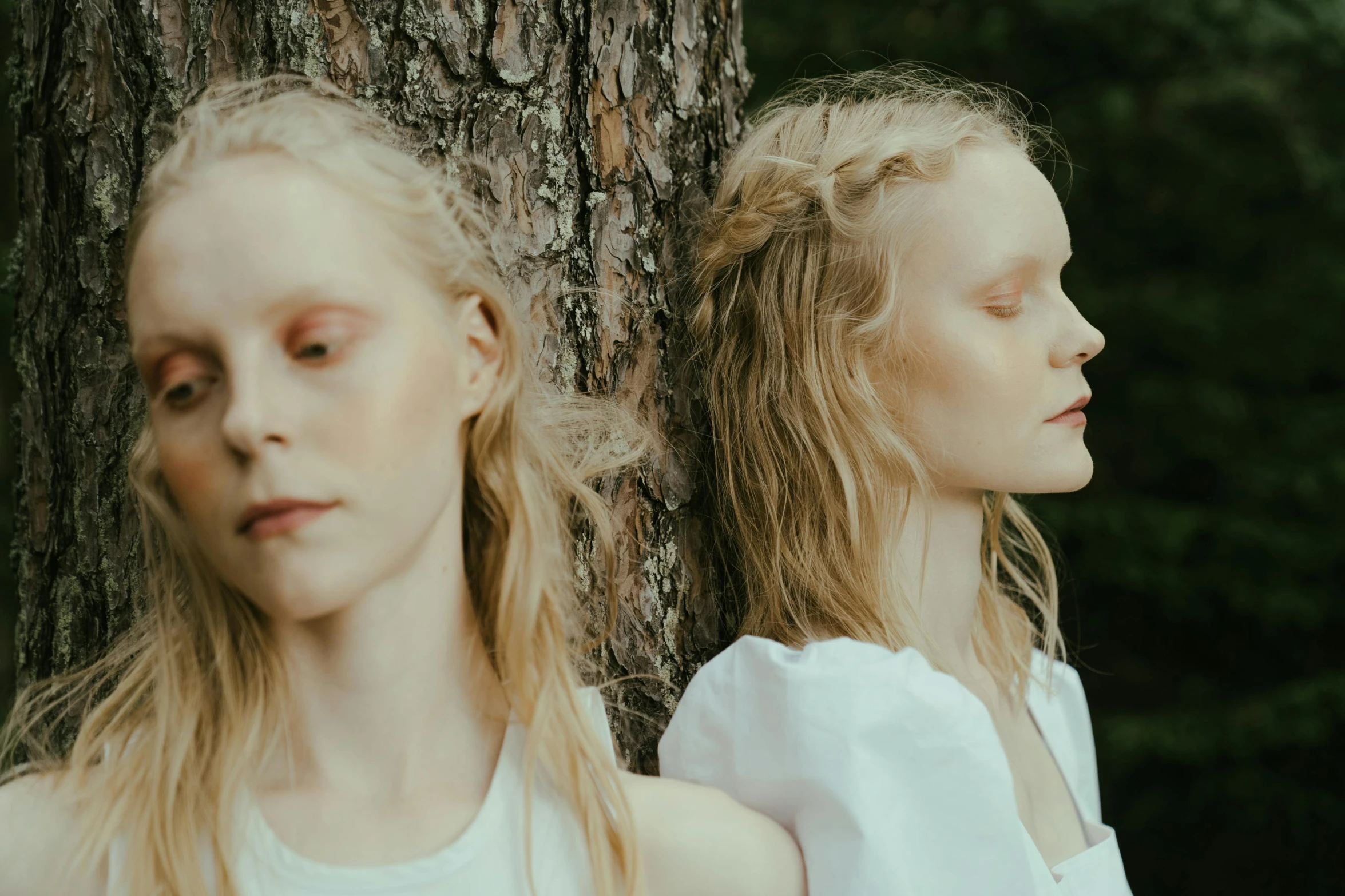 two blonde haired women next to tree looking sad