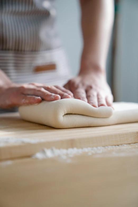 a person kneading an uncooked dough on a wooden table