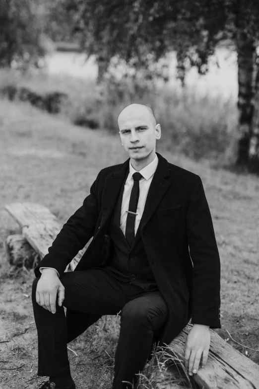 a bald man in a suit and tie sitting on a tree log