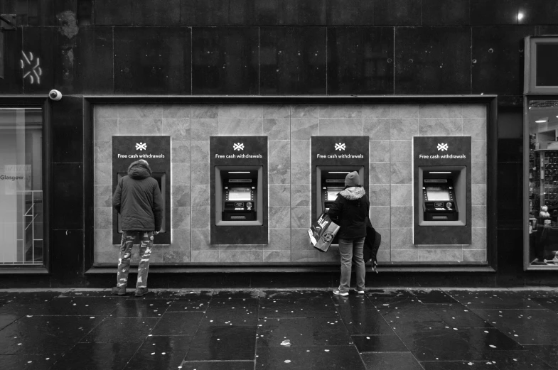 two people with cell phones outside of atms