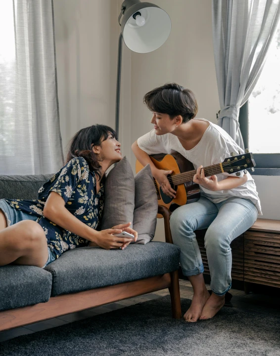 two people sitting on a couch and one man playing guitar