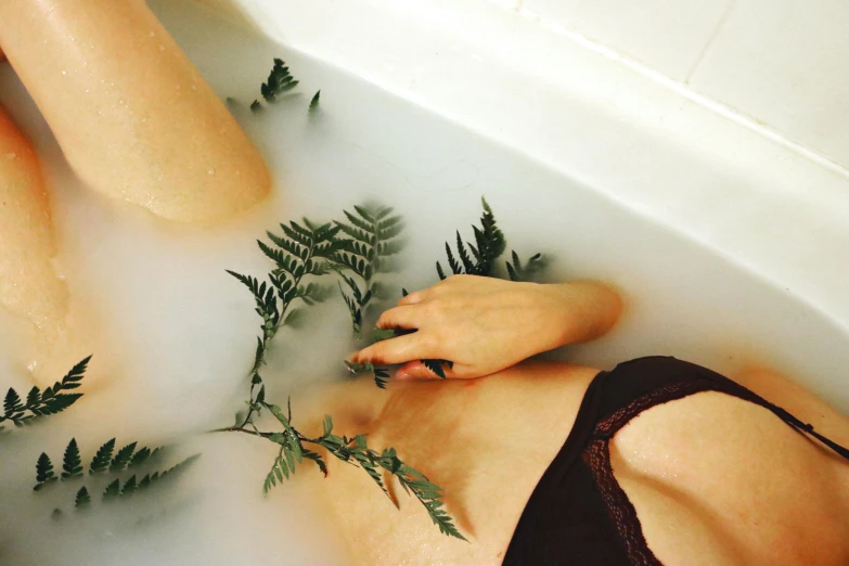 the young woman is laying in the bathtub with green plants growing on it