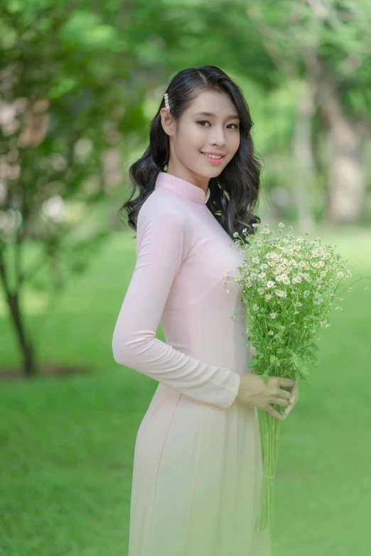 an attractive young woman in a pale dress holds flowers