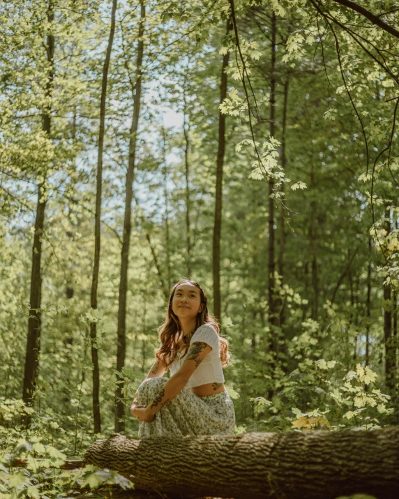 the young woman is sitting on a tree trunk in a forest