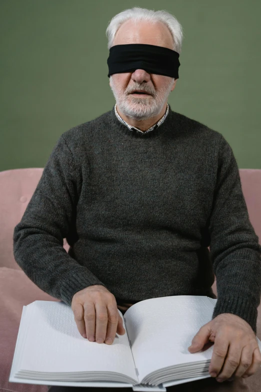 a man wearing a blindfold holds a book with his hands and reads