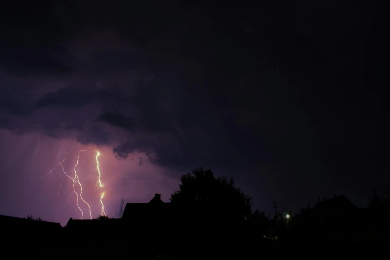 lightning is seen in the dark sky over houses