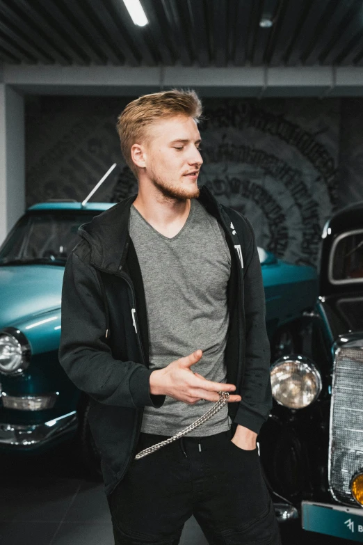 a young man in a black leather jacket standing by an old car