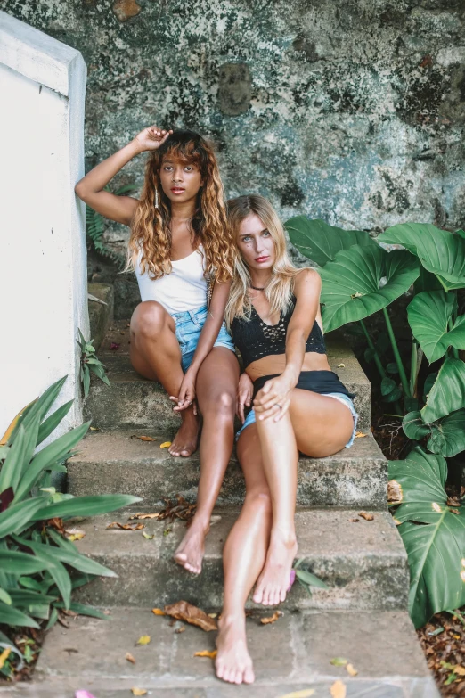 two woman sitting on steps outside of a stone wall