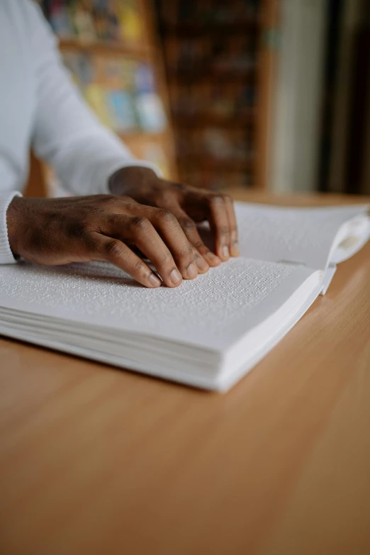 a person sitting at a wooden table with their hands on a book
