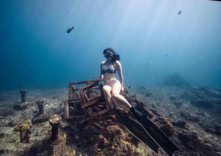 a bikini clad woman sits on a sunken boat