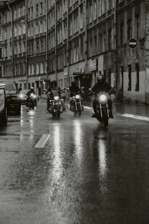 a group of motorcycle riders driving down a wet street