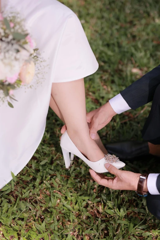 a newly wed couple hold their wedding shoes and they both wear high heels