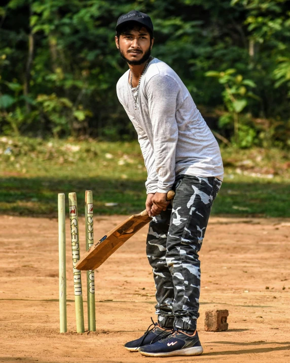 a young man wearing camo pants, black cap and white shirt playing cricket