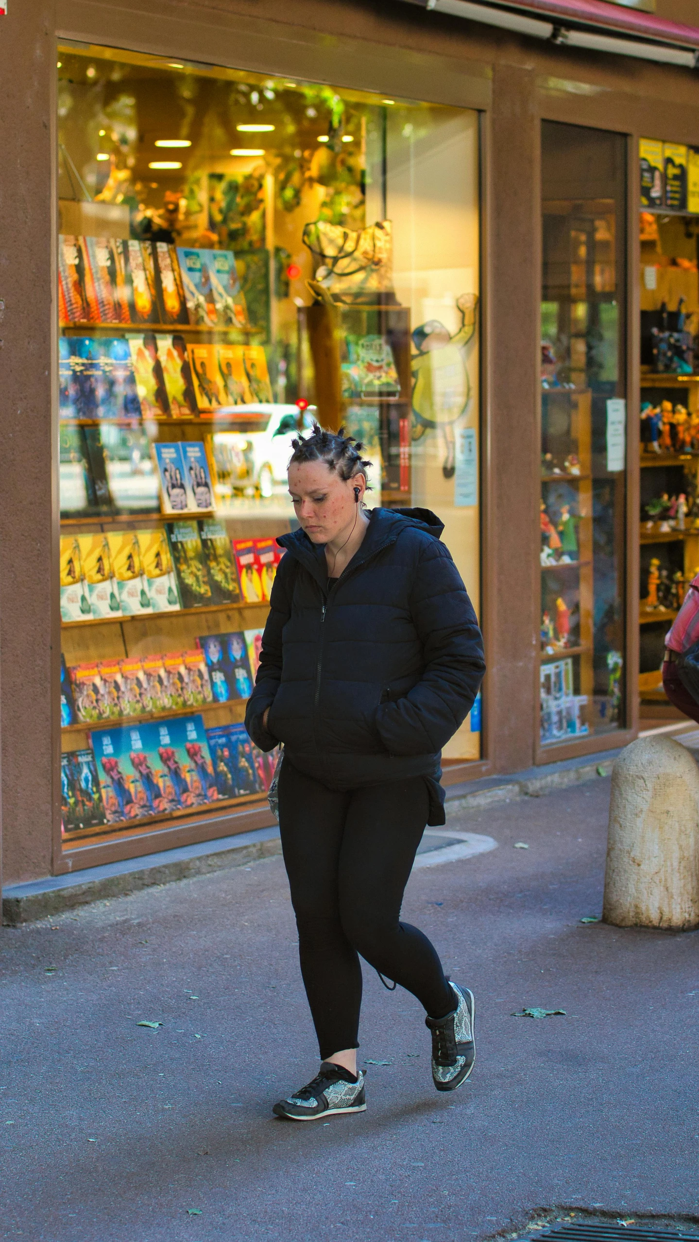 a woman walking down the street wearing a black jacket and sports shoes