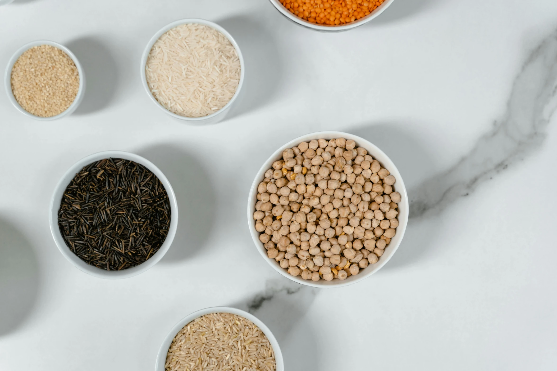 five bowls containing wheat, chickpeas, and sesame seeds