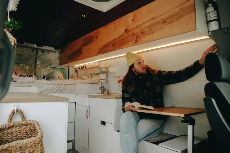 a man with long hair sitting in a kitchen while holding a piece of paper