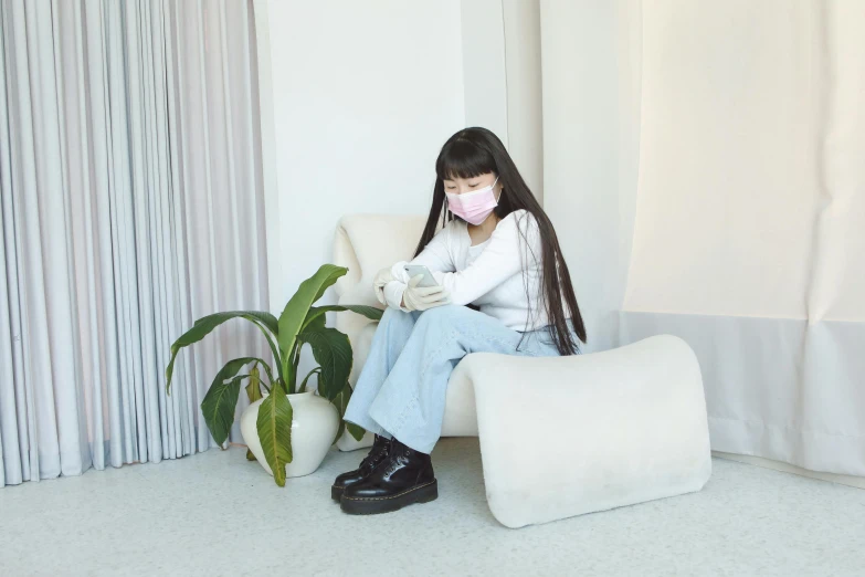 a girl with long hair wearing a face mask is sitting on a sofa and drinking from a cup