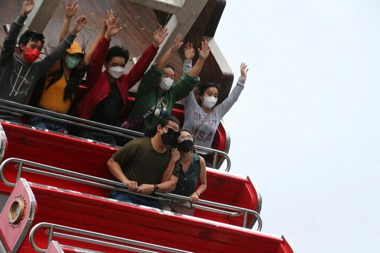 a group of people in a red double decker bus waving and wearing masks