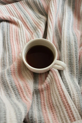 a cup of black coffee on a striped blanket