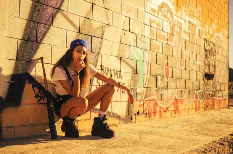 a young lady is sitting next to a graffiti covered wall and talking on her cellphone