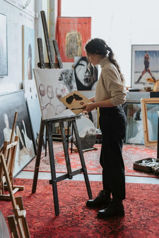 an artist with a dog sits in front of an easel as she draws a portrait